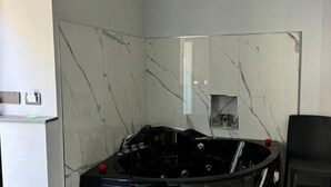 Ein modernes Badezimmer mit Marmorwand, einer schwarzen Badewanne und einem kleinen Ablagebrett mit Gläsern.