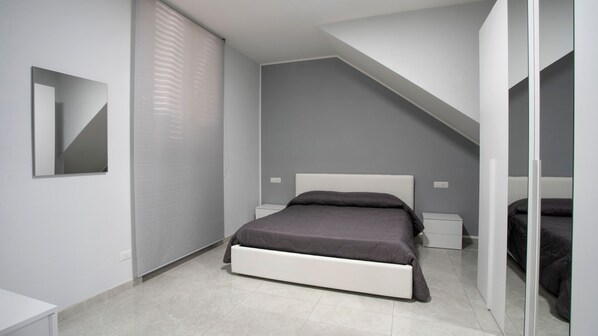 A modern bedroom with a bed, bedside tables, a mirror, and a sloped ceiling.