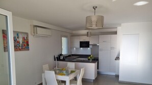 A modern kitchen with white cabinetry, a central island, and a dining area with white chairs. - Apt With Pool   Magnificent Sea View, 80m To Beach (Sainte-Maxime)