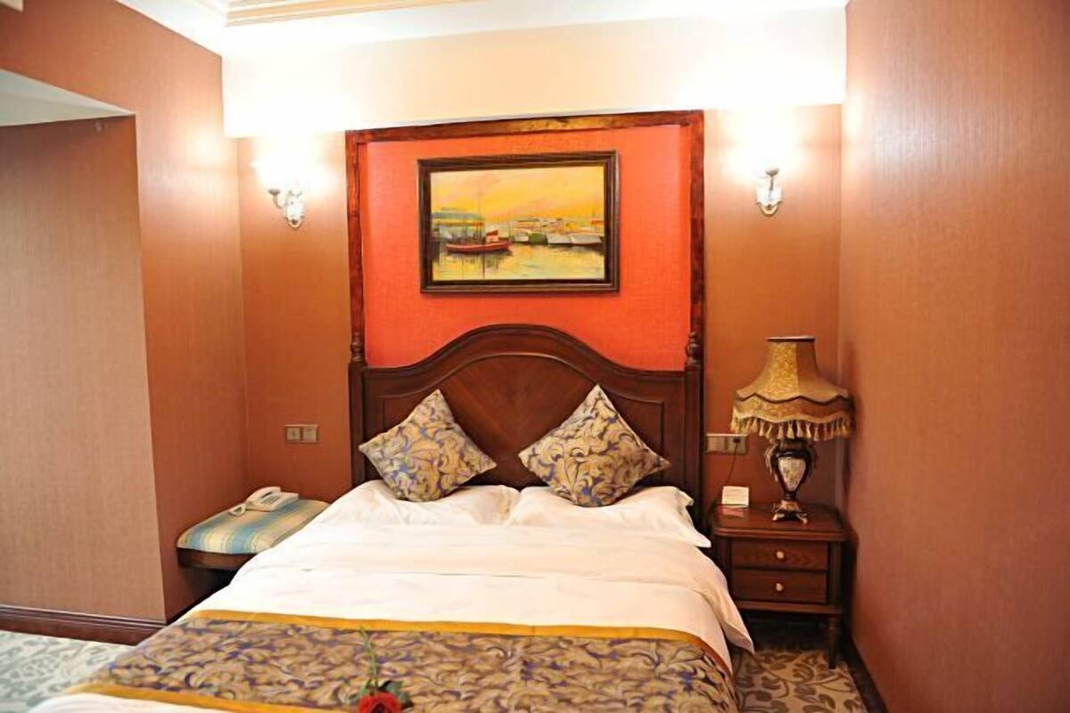A hotel room with a bed, a nightstand, a lamp, and a painting on the wall.