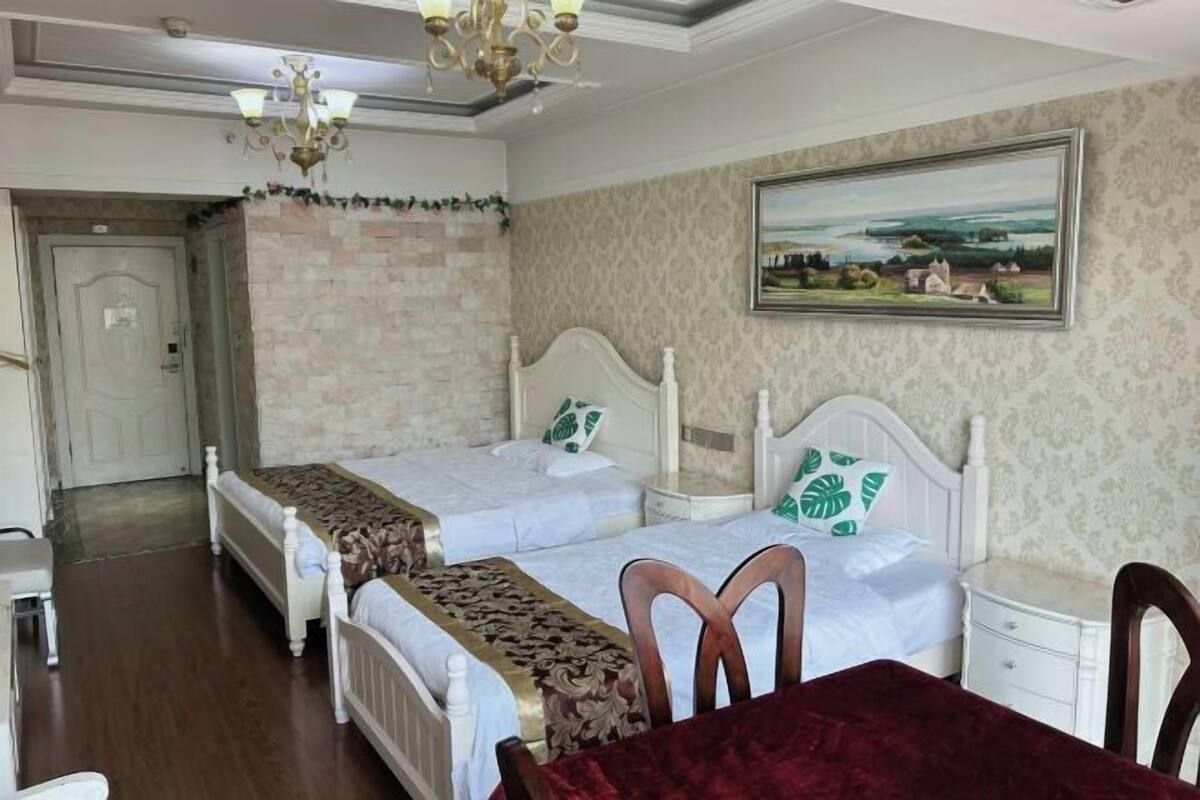 A hotel room with two beds, a dining table, and a painting on the wall.