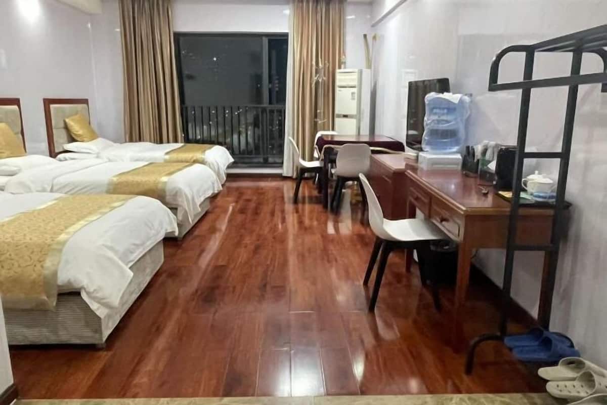 A hotel room with two beds, a desk, a chair, a water dispenser, and a view of the outside.
