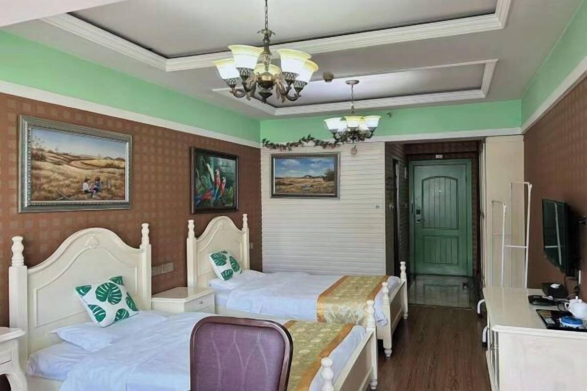 A hotel room with two beds, a desk, a chair, a television, and artwork on the walls.