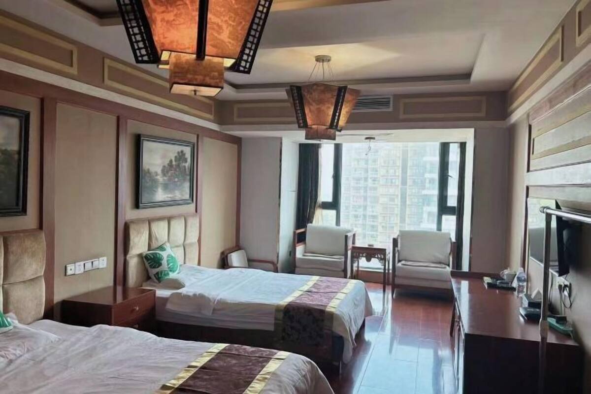 A hotel room with two beds, a desk, a chair, a television, and a large window with a city view.