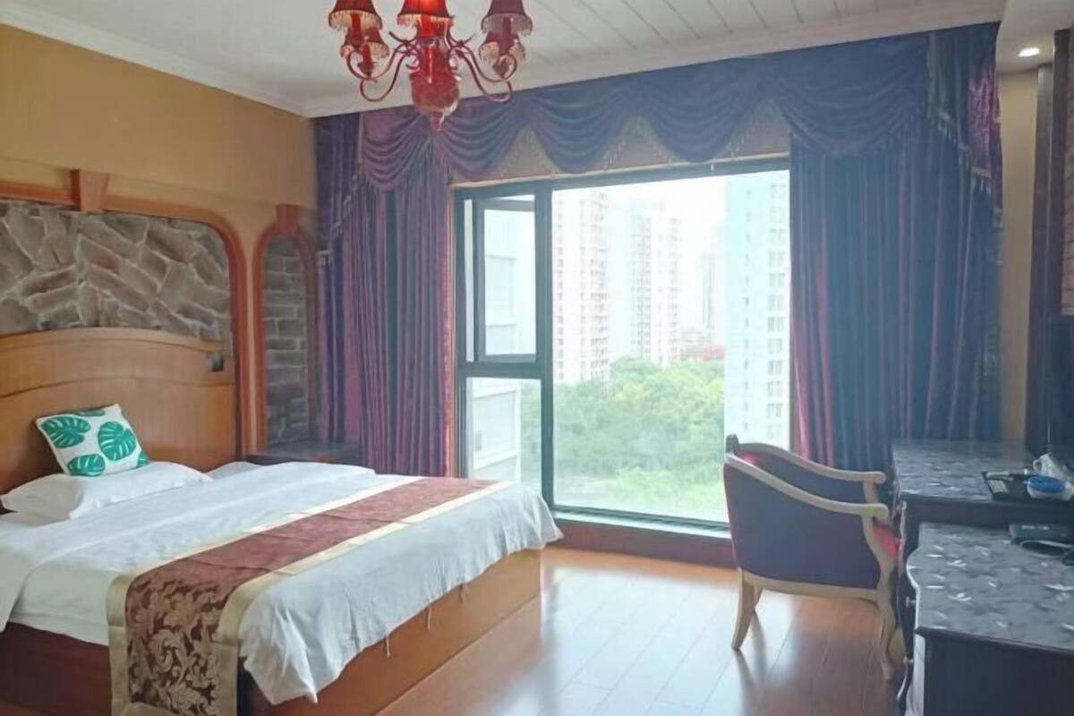 A hotel room with a bed, a desk, a chair, a stone accent wall, and a large window with curtains.