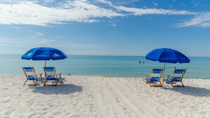 A beach with two blue umbrellas and four beach chairs.