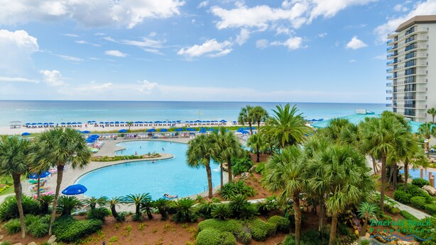 A resort with a pool, palm trees, and a view of the ocean.