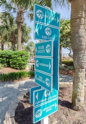 A directional sign with arrows pointing to various hotel amenities including the club, hair salon, restrooms, tiki airbrush, conference center, and adventure zone.