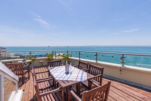 Una terraza de madera con una mesa y sillas, que da a un cuerpo de agua con una orilla lejana.