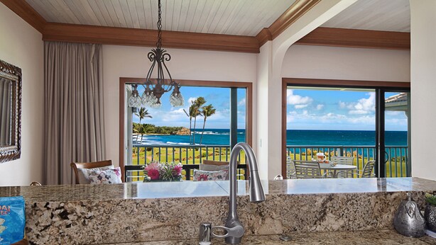 A kitchen with a sink, a view of the ocean, and a dining area with outdoor furniture. - Poipu Sands 522 Gorgeous Oceanfront  By Suite Paradise (Koloa)