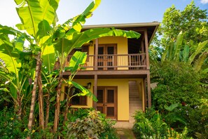 Ein zweistöckiges Haus mit Balkon, umgeben von üppiger Vegetation und Bananenstauden.