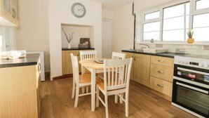 A modern kitchen with wooden cabinets, a dining table with chairs, a built-in oven, and a window with a view. - 1 Woodhouse Cottages (Hull)