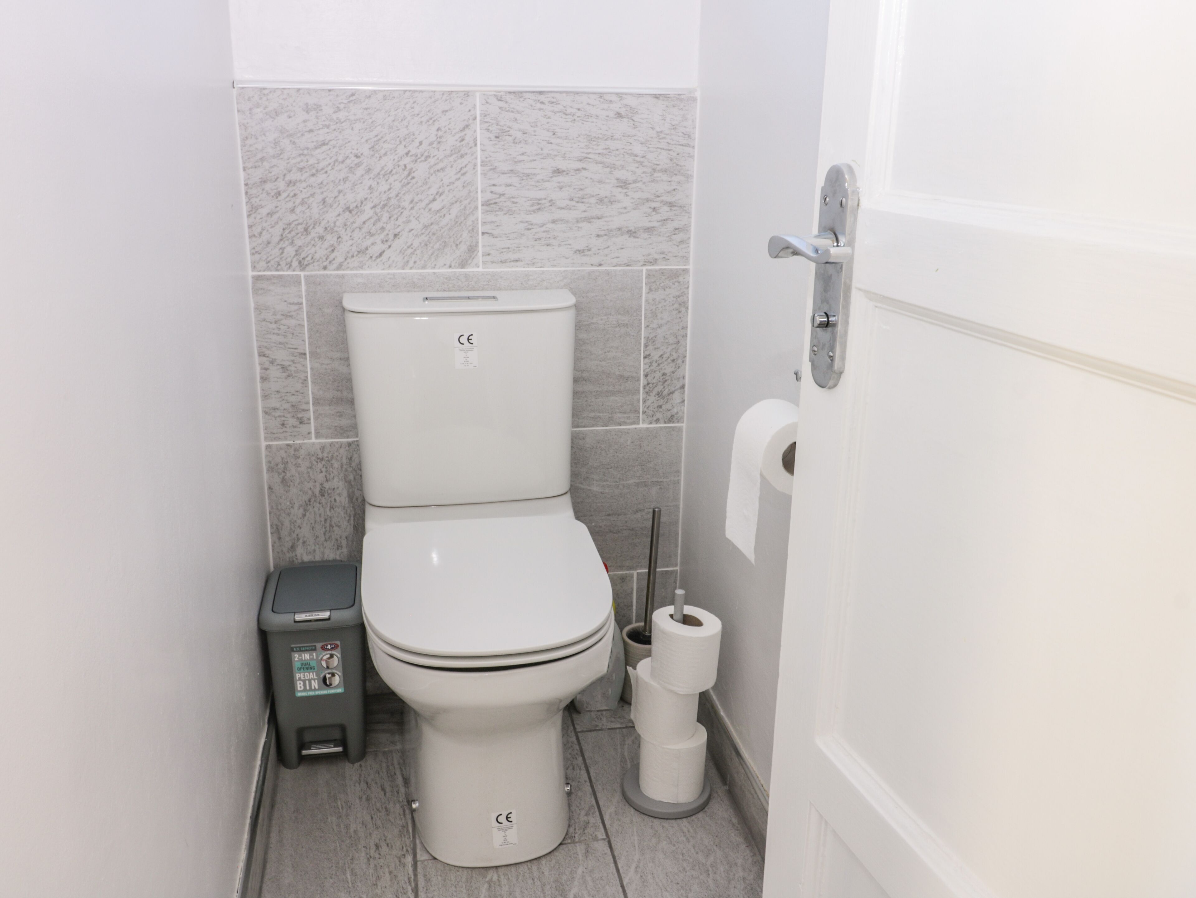 Et badeværelse med toilet, skraldespand og toiletpapirholder.