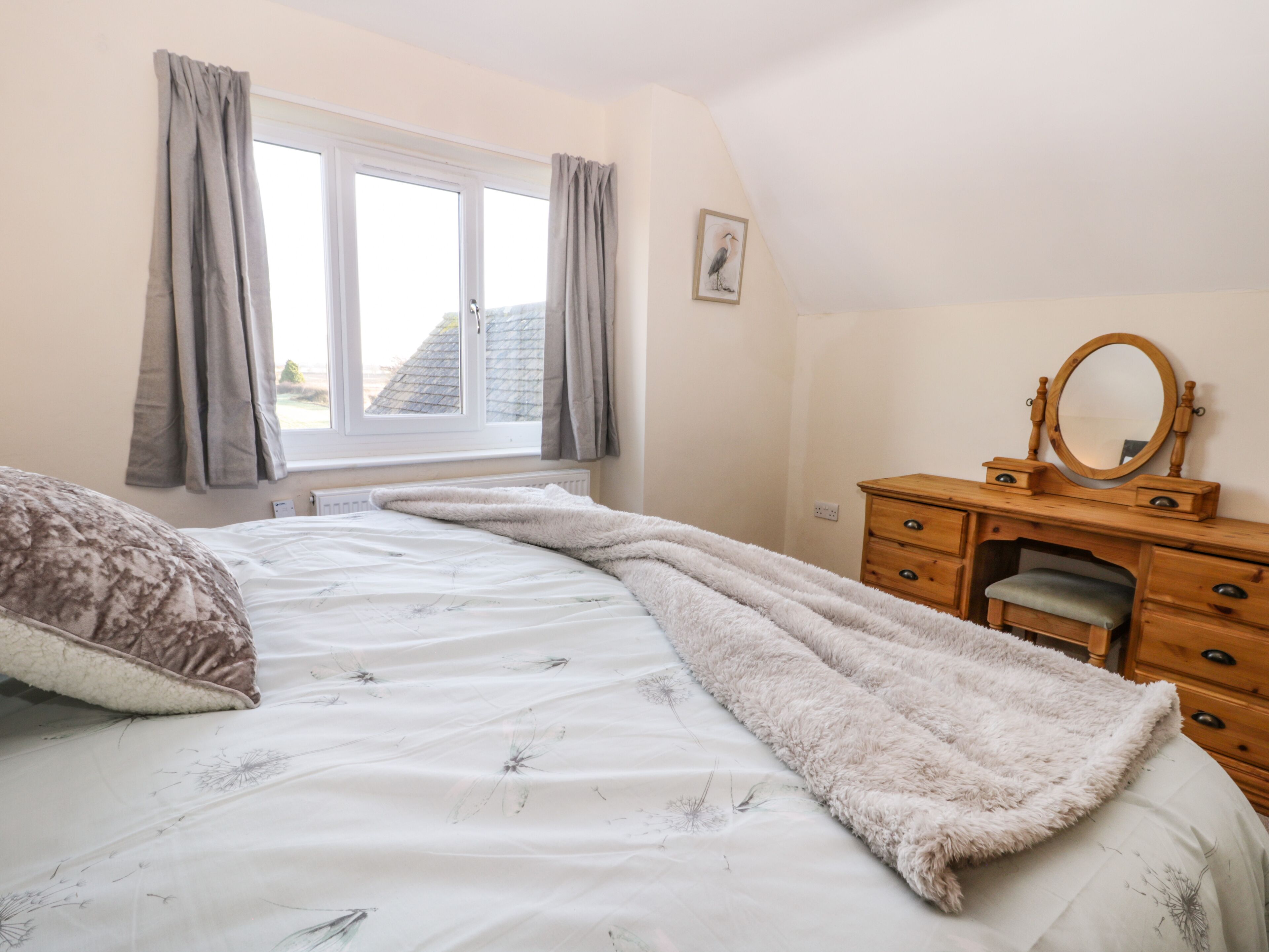 A bedroom with a bed, a wooden dresser with a mirror, and a window with curtains.