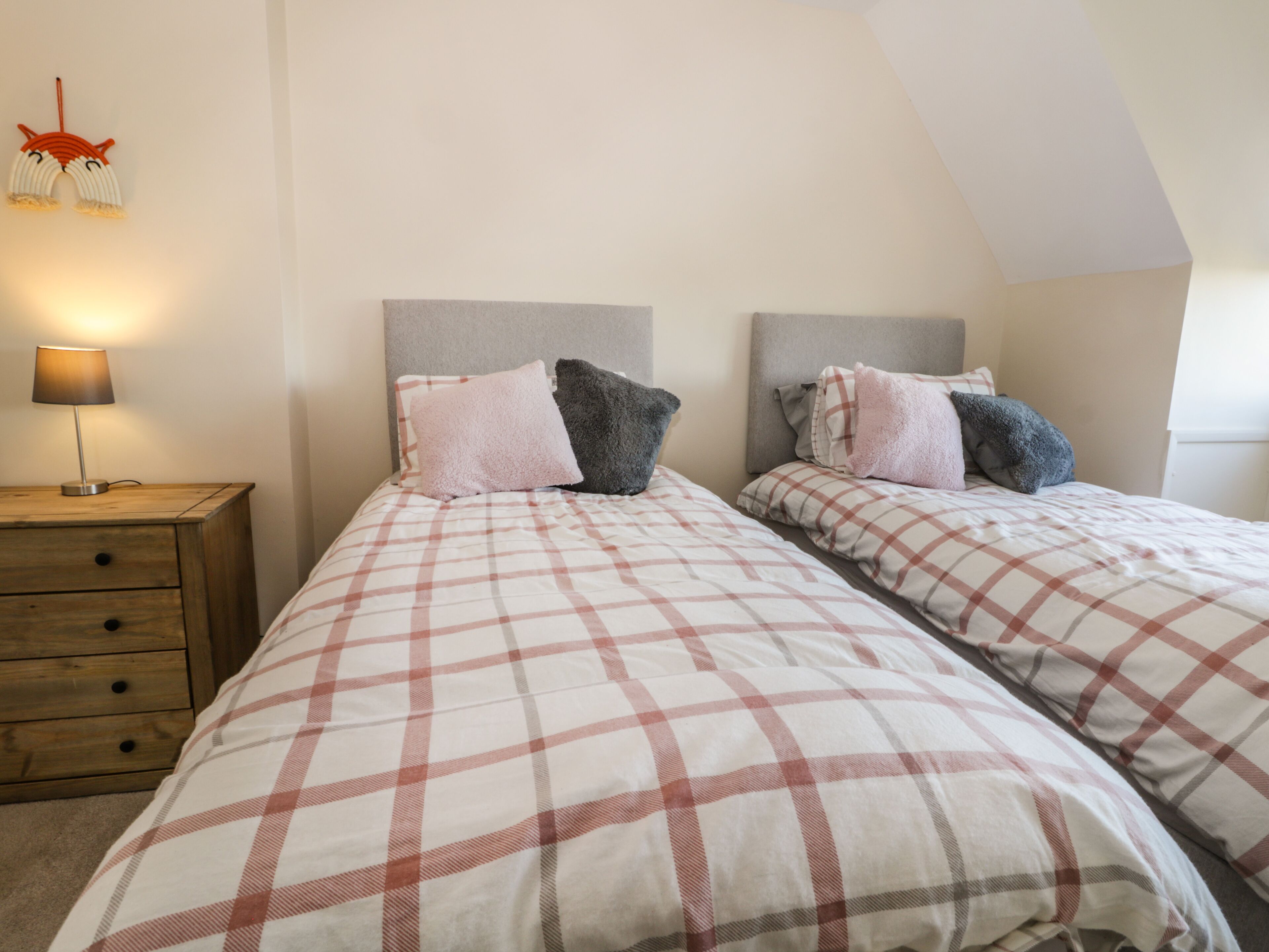 A bedroom with two beds, each with a checkered bedspread, a nightstand with a lamp, and a wall-mounted decoration.