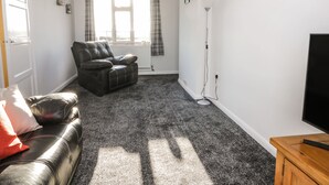 A living room with a leather sofa, a black leather chair, a wooden TV stand, a floor lamp, and a window with curtains. - 1 Woodhouse Cottages (Hull)