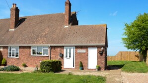 A brick cottage with a white door, a sign reading "Woodhouse Cottages," and a small garden with grass and flowers. - 1 Woodhouse Cottages (Hull)