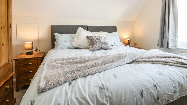 A bedroom with a large bed, two bedside tables, a wardrobe, and a window with curtains. - 1 Woodhouse Cottages (Hull)