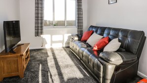 A living room with a leather sofa, a wooden TV stand, and a window with curtains. - 1 Woodhouse Cottages (Hull)