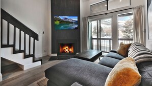 Een moderne woonkamer met een open haard, een grote televisie en een bank met uitzicht op de omgeving.