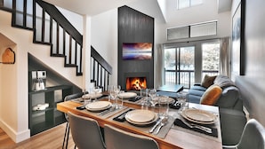 Een moderne eetruimte met een houten tafel voor vier personen, een open haard en een trap.