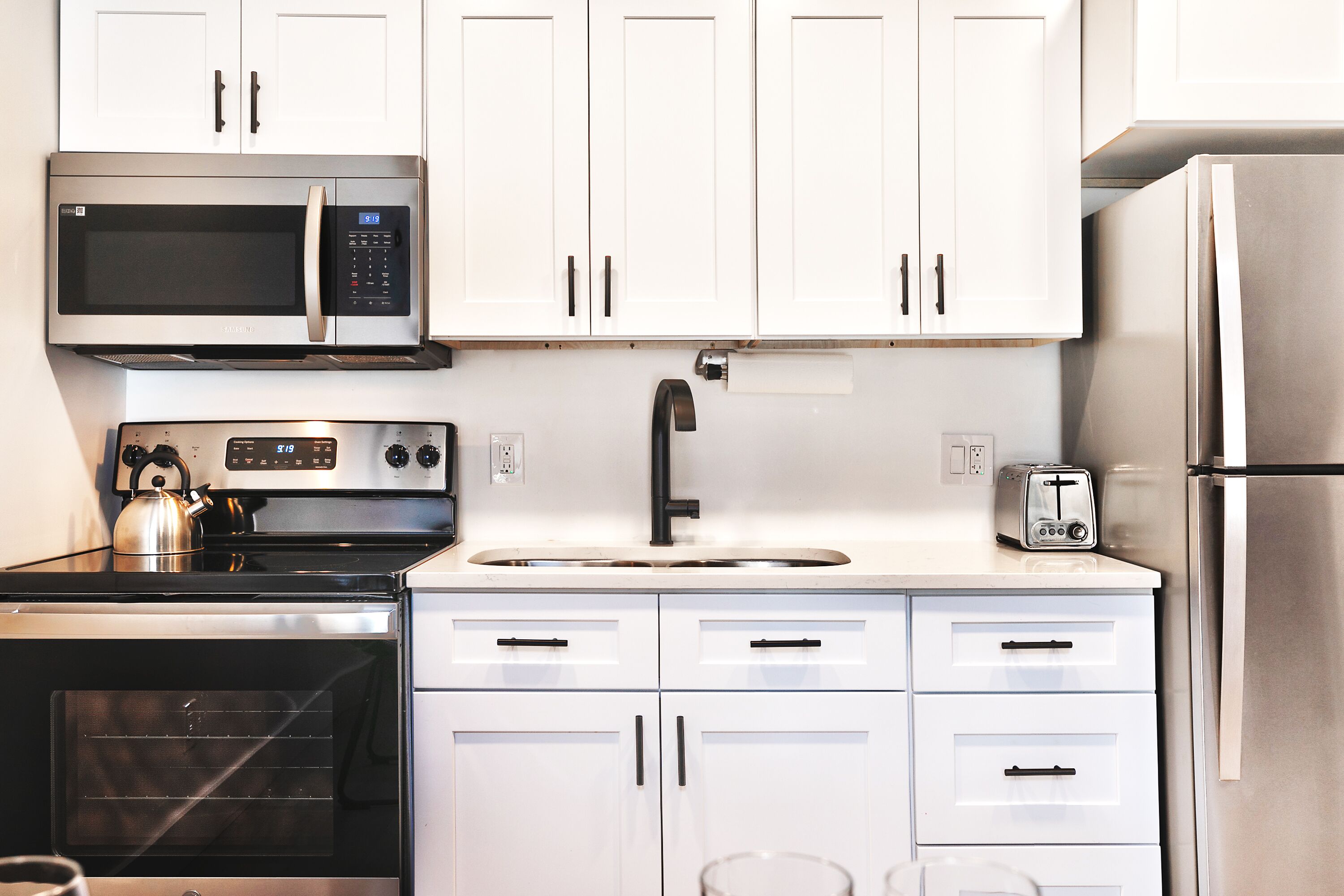 A modern kitchen with white cabinets, a stainless steel microwave, oven, and refrigerator.