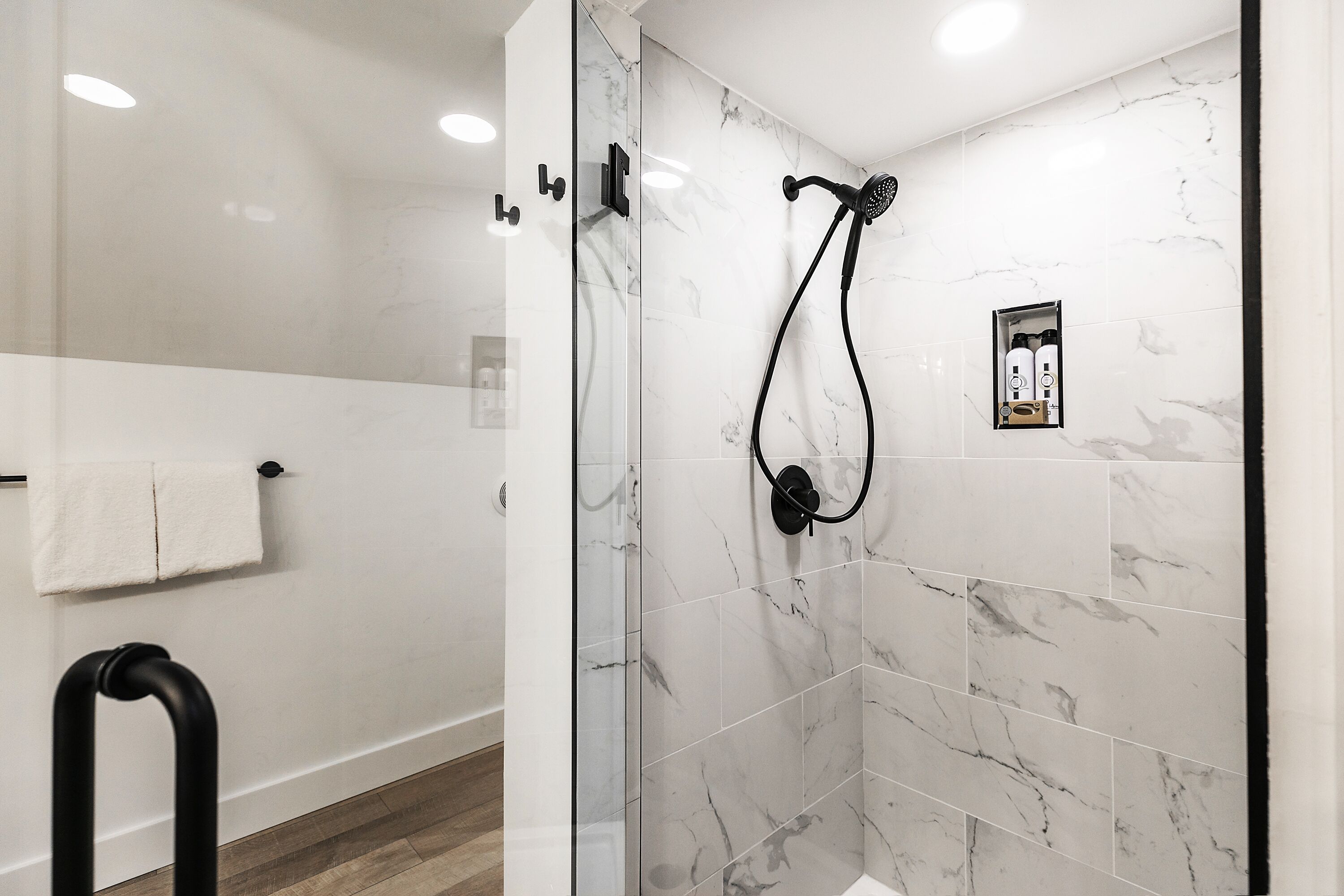 A modern bathroom with a glass-enclosed shower, marble tiles, and a black towel rack.