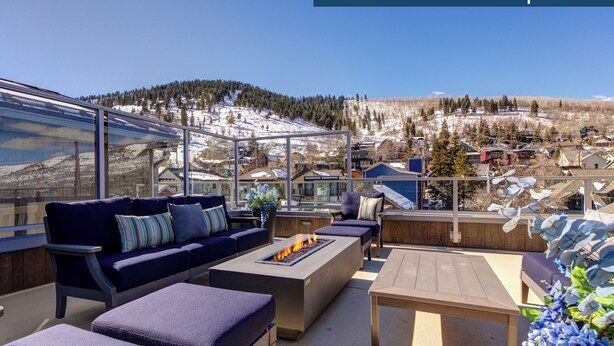 Terraza en la azotea con mobiliario exterior, un brasero y vistas a un pueblo de montaña nevado.