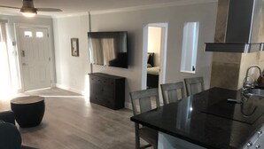 Una cucina moderna con un piano di lavoro nero, mobili bianchi e forno integrato. C'è una zona pranzo con tavolo e sedie, e un ventilatore a soffitto.
