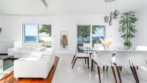A modern living room with a white sofa, a glass dining table, and a view of the sea. - Seaview Villa MaToLi with heated 50sqm pool and 4 bedrooms, close to Split (Podstrana)