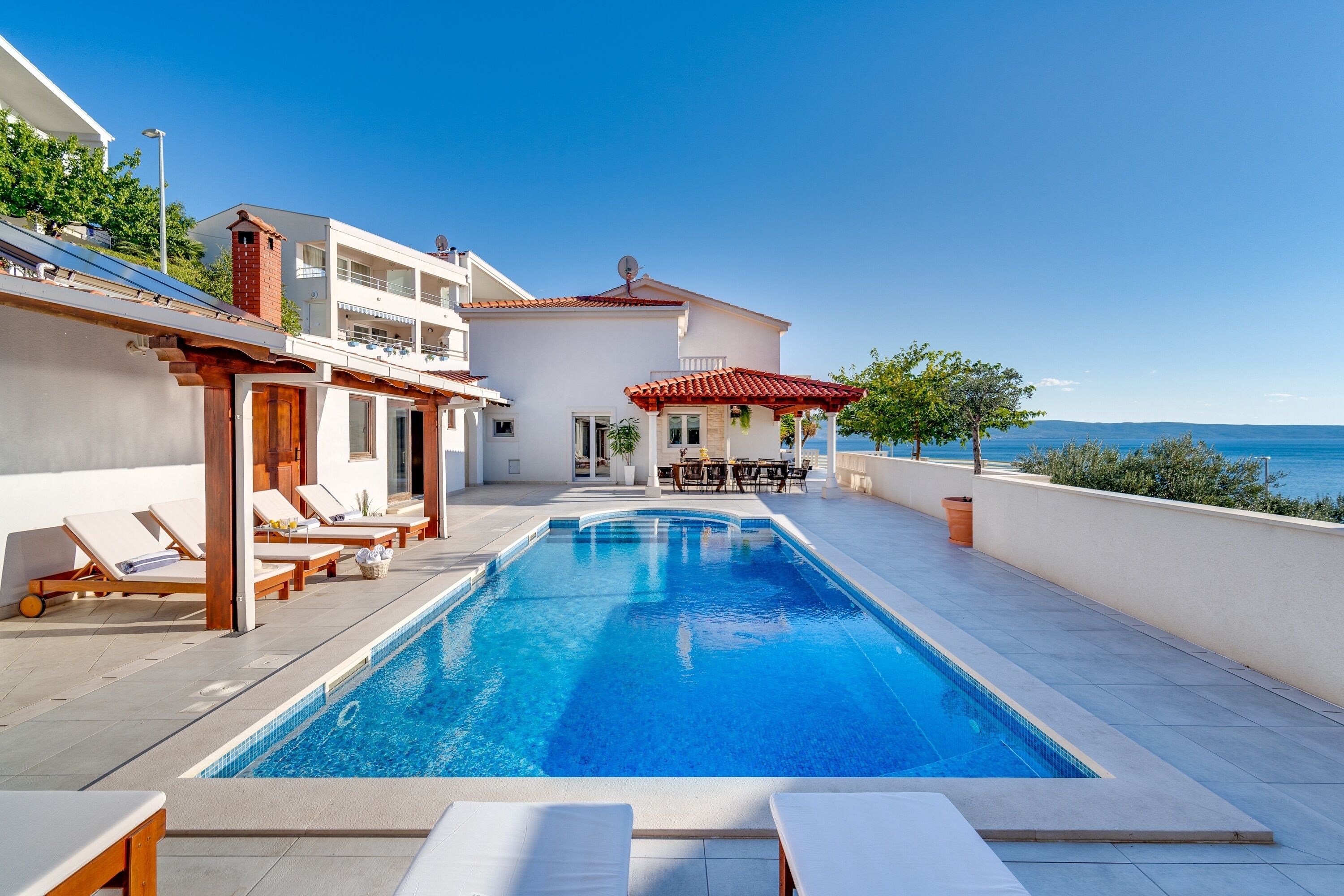 A swimming pool with lounge chairs, a dining area, and a view of the sea.