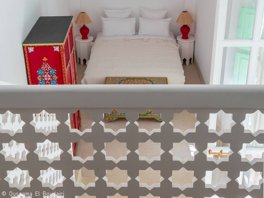 Un dormitorio con una cama, dos mesitas de noche, un objeto decorativo rojo, un farol colgante y una puerta blanca.