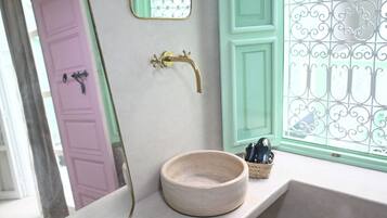 A bathroom with a round sink, a mirror, a window with a green door, and a decorative metal screen.