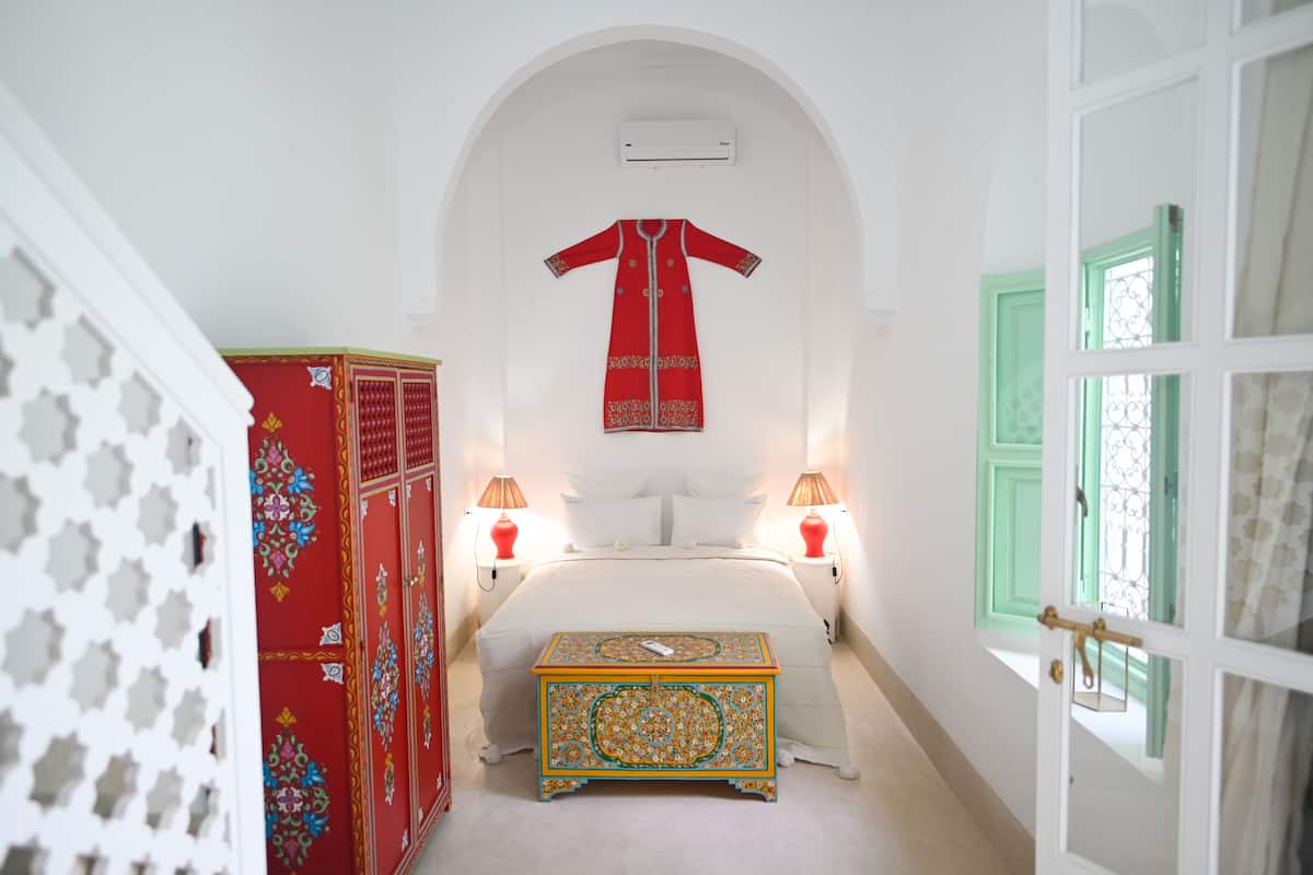 Un dormitorio con cama, lámparas de noche, perchero y cómoda decorativa.