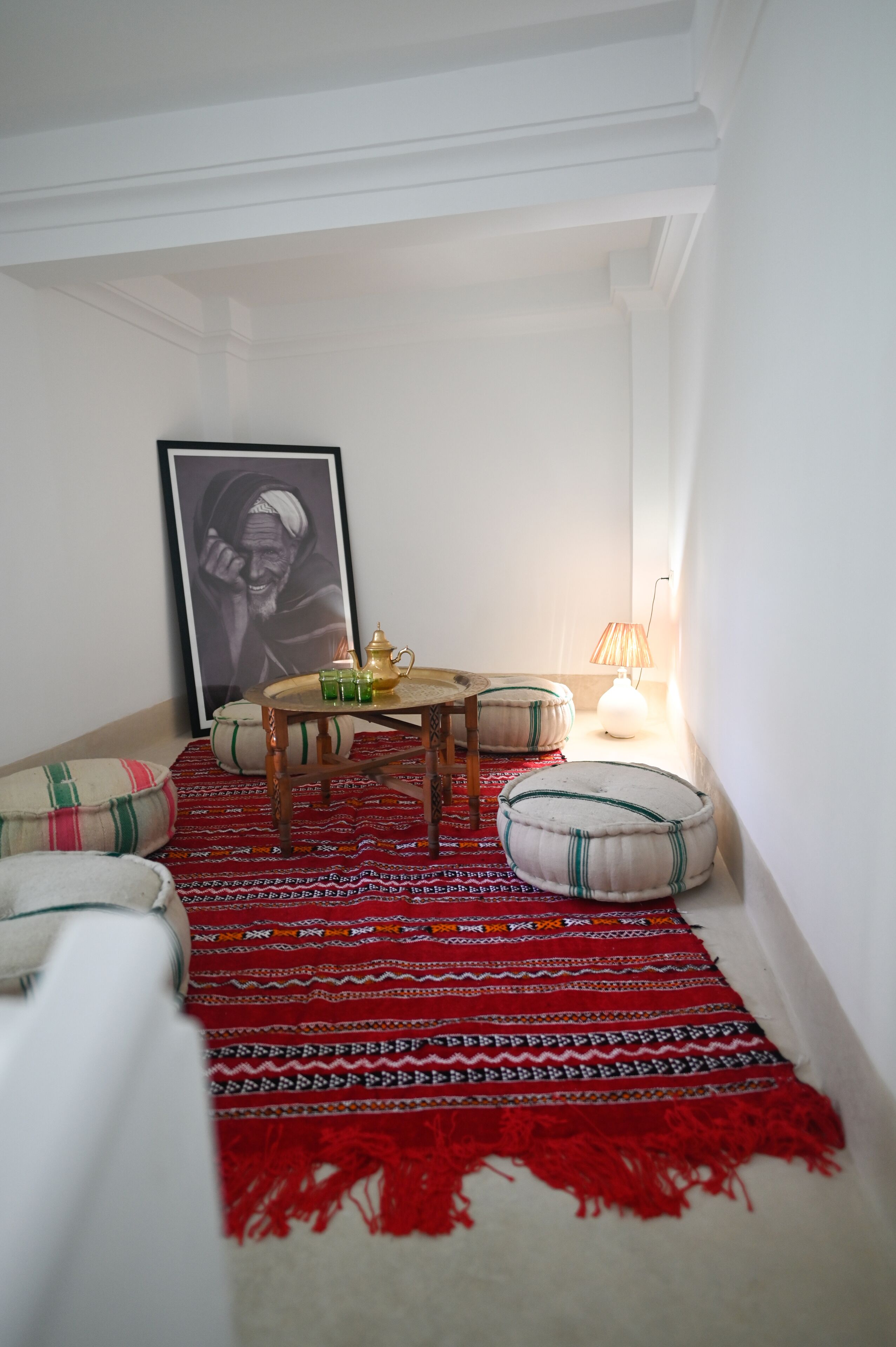 A cozy room with a red patterned rug, a small round table with a teapot, and a framed picture on the wall.