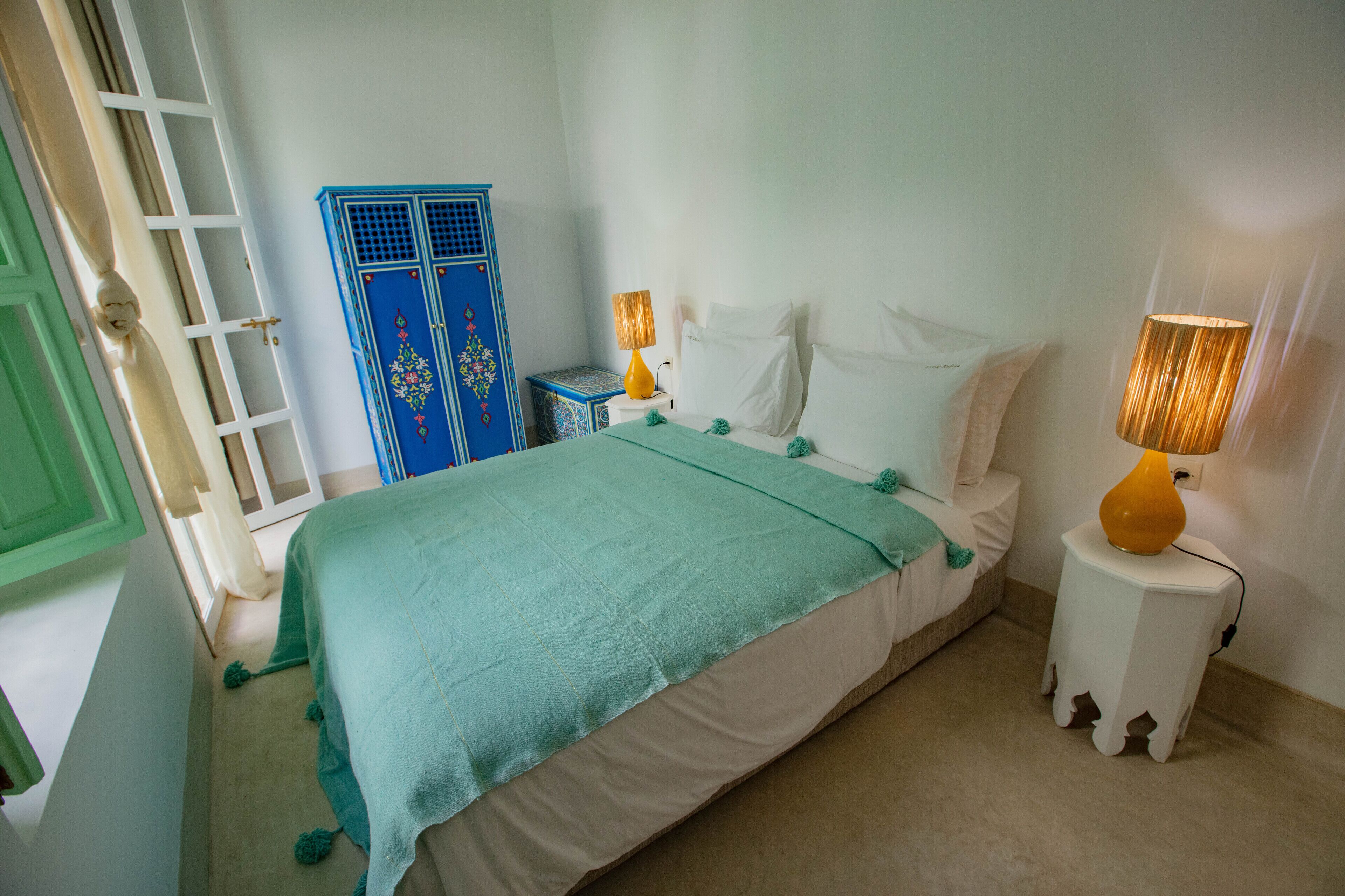 A bedroom with a bed, two bedside lamps, a blue wardrobe, and a green door.
