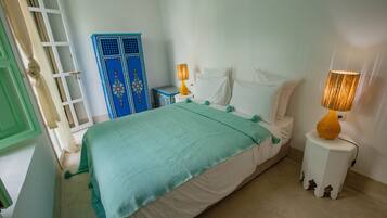 A bedroom with a bed, two bedside lamps, a blue wardrobe, and a green door.