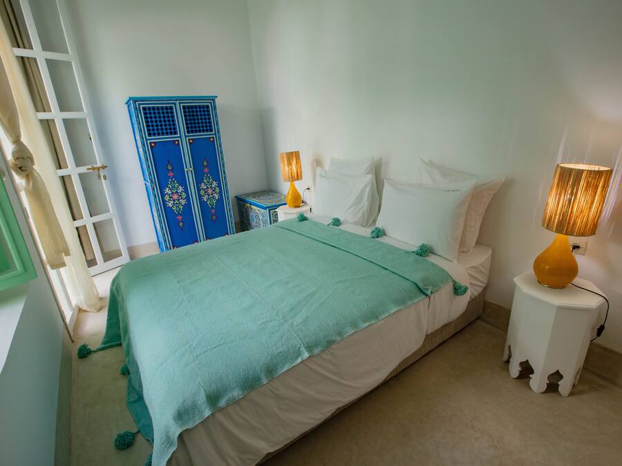 A bedroom with a bed, two bedside lamps, a blue wardrobe, and a green door.