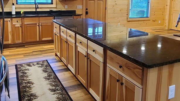 L’intérieur d’un chalet en bois comprend une cuisine avec des meubles en bois, un plan de travail noir et des luminaires suspendus.