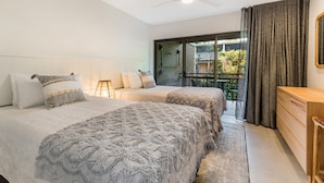 Quarto com duas camas, mesa de cabeceira, cômoda e vista para o exterior.