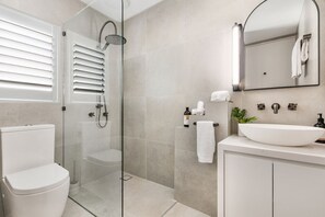 A modern bathroom with a glass-enclosed shower, a white toilet, a sink with a large mirror, and a towel rack. - Sundown Lodge 4 (Noosa Heads)