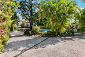 Un quartier résidentiel doté d’une piscine, entourée d’une végétation luxuriante, et d’un chemin piétonnier dallé.