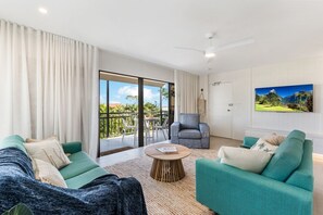 A spacious living room with teal sofas, a round coffee table, and a large sliding glass door leading to an outdoor area.