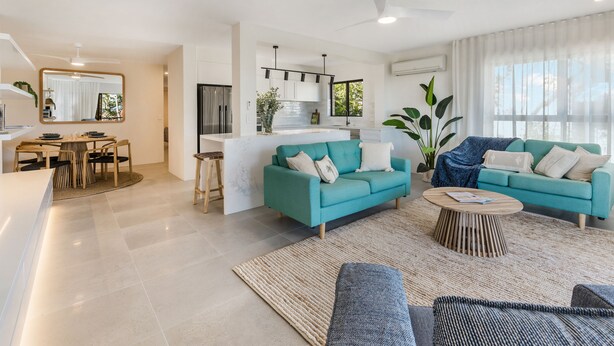 Uma sala de estar moderna com um sofá azul-turquesa, uma mesa de centro e uma área de jantar com mesa e cadeiras de madeira.