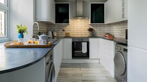 Een moderne keuken met witte kastjes, een ingebouwde oven, een wasmachine en een ontbijtbakje op het aanrecht.