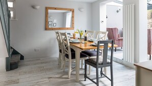 Een eetgedeelte met een houten tafel, witte stoelen en een spiegel aan de muur.