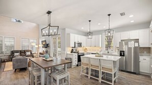 A modern kitchen with white cabinetry, stainless steel appliances, and a wooden dining area. - DISCOUNTED!~FREE Activities~6 SEAT GOLF CART~Pool~Hot tub~pets considered (Miramar Beach)