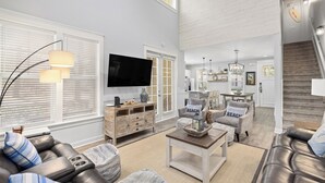 A modern living room with a sofa, ottoman, and coffee table. There is a TV mounted on the wall, a wooden cabinet, and a staircase leading to another level. - DISCOUNTED!~FREE Activities~6 SEAT GOLF CART~Pool~Hot tub~pets considered (Miramar Beach)