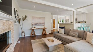 Amplia sala de estar con chimenea, un sofá modular grande, una mesa de centro y vista a la cocina.