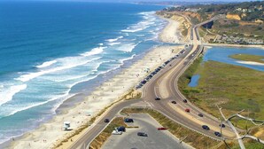 Carretera costera con acceso a la playa, vehículos y una torre de salvavidas.
